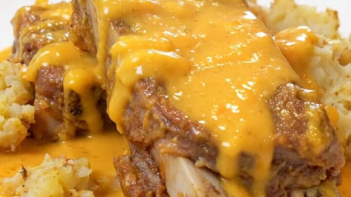 Cheesy scalloped potatoes and tender country pork ribs on a white plate, coated in creamy cheddar sauce with light steam