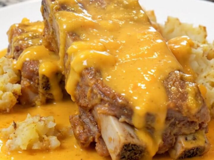 Cheesy scalloped potatoes and tender country pork ribs on a white plate, coated in creamy cheddar sauce with light steam