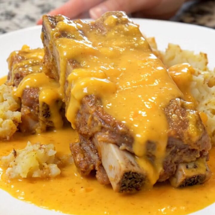 Cheesy scalloped potatoes and tender country pork ribs on a white plate, coated in creamy cheddar sauce with light steam