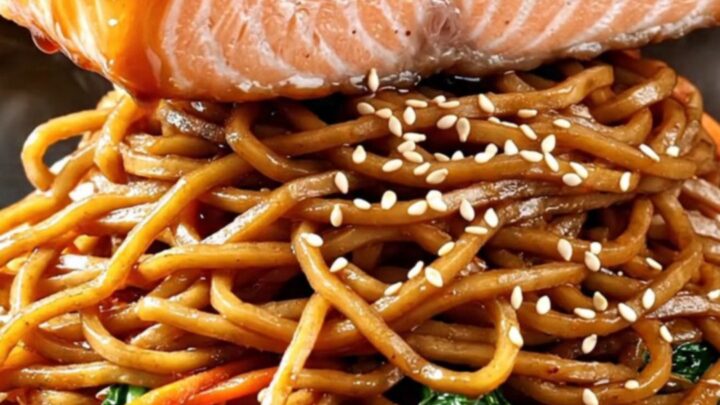 Crispy-skinned teriyaki salmon fillet glazed in glossy sauce over a steaming bowl of yakisoba noodles with charred bok choy