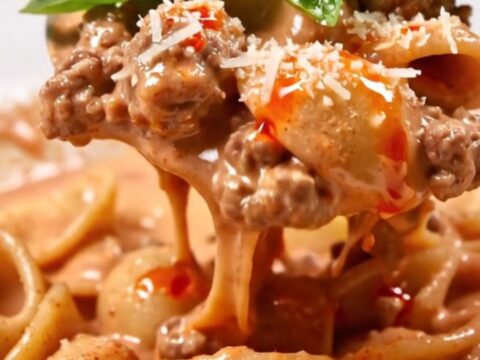 Orecchiette in creamy pink vodka Bolognese with tiny meatballs, torn basil and a drizzle of chili oil in a white bowl