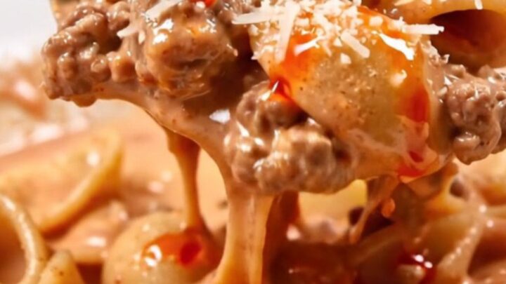 Orecchiette in creamy pink vodka Bolognese with tiny meatballs, torn basil and a drizzle of chili oil in a white bowl