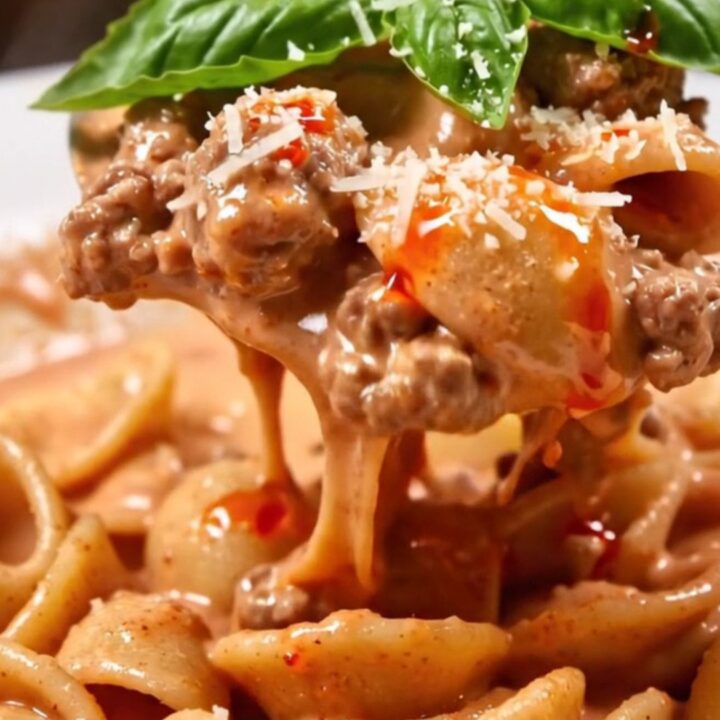 Orecchiette in creamy pink vodka Bolognese with tiny meatballs, torn basil and a drizzle of chili oil in a white bowl