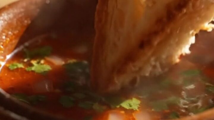 Birria grilled cheese pulled apart in slow motion, golden cheese strings soaked in glossy red birria oil between thick
