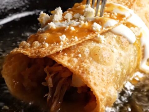Crispy birria chimichanga on a plate, smothered in red consomé with crema and cotija