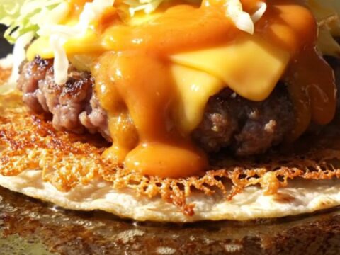 Crispy smash burger taco folded in half, lacy brown beef edge, melted American cheese and orange burger sauce drizzle