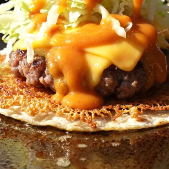 Crispy smash burger taco folded in half, lacy brown beef edge, melted American cheese and orange burger sauce drizzle
