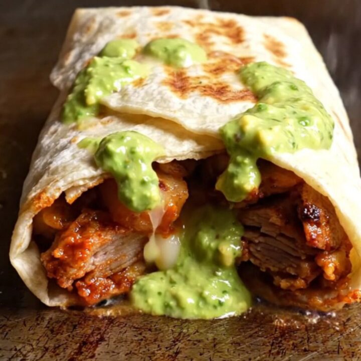 Al pastor pork burrito cut in half showing red pork, creamy elote rice, charred corn and melted Oaxaca cheese