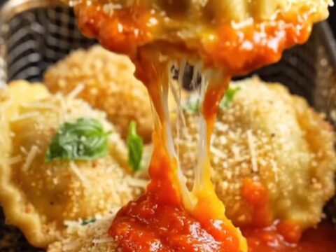 Golden toasted air fryer ravioli piled on a platter with grated Parmesan, fresh basil and a bowl of warm marinara for dunking