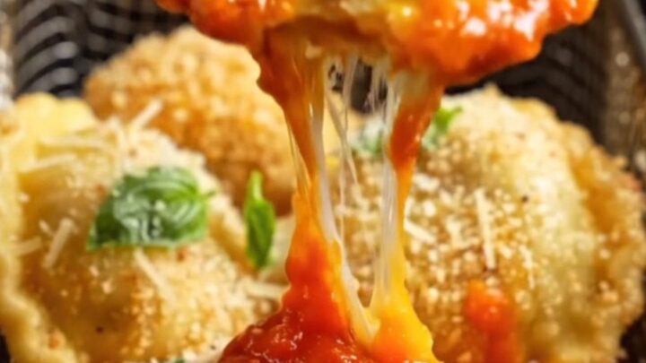 Golden toasted air fryer ravioli piled on a platter with grated Parmesan, fresh basil and a bowl of warm marinara for dunking