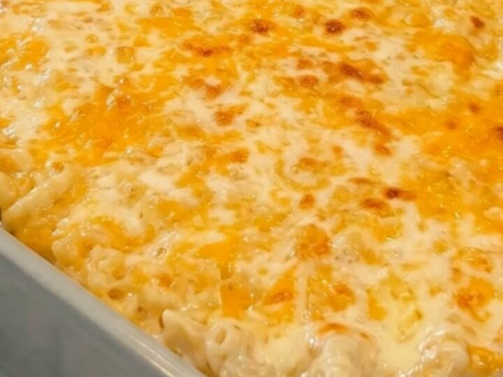 Baked mac and cheese in a grey ceramic dish with a golden crust and a spatula lifting a gooey, steaming scoop