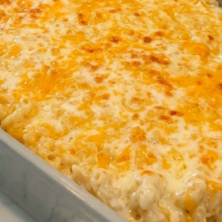 Baked mac and cheese in a grey ceramic dish with a golden crust and a spatula lifting a gooey, steaming scoop