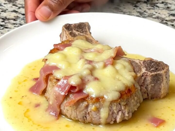 Tender slow-cooked pork chop topped with soft ham and melted Swiss cheese under a thick creamy sauce