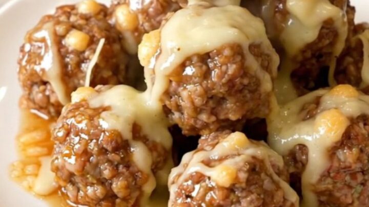 Glossy garlic parmesan beef meatballs coated in melted cheese sauce, steaming on a white plate