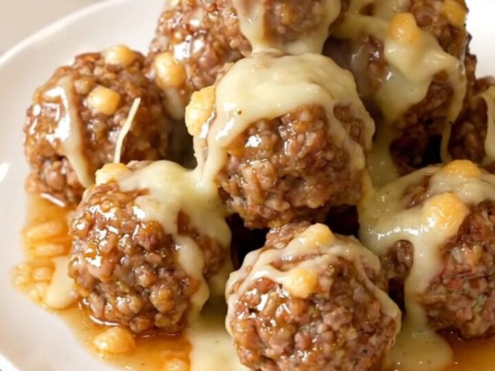 Glossy garlic parmesan beef meatballs coated in melted cheese sauce, steaming on a white plate