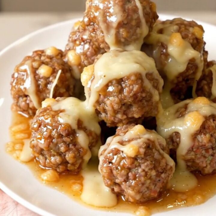 Glossy garlic parmesan beef meatballs coated in melted cheese sauce, steaming on a white plate