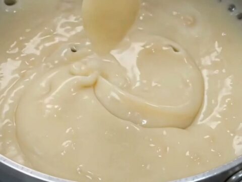 Glossy off-white coconut pudding in a white bowl with a spoon lifting a thick ribbon