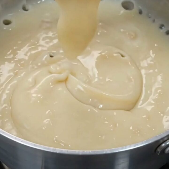 Glossy off-white coconut pudding in a white bowl with a spoon lifting a thick ribbon