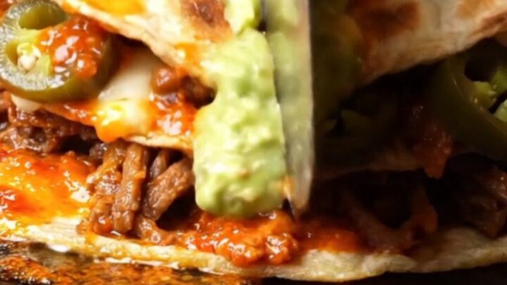 Double-stacked lamb birria pizzadilla cut into wedges with oozing Oaxaca cheese and avocado salsa drizzle