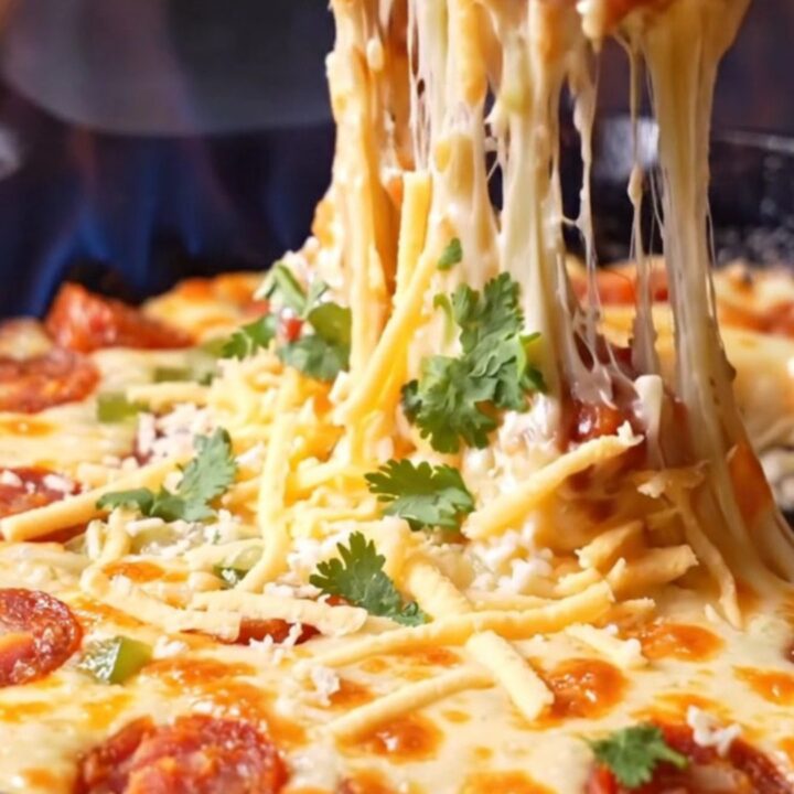 Cast-iron skillet of molten chorizo queso fundido with a long cheese pull lifted on a tortilla chip
