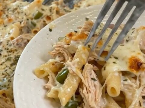 Mississippi chicken casserole with pasta and melted cheese lifted from a glass baking dish with a spatula, steam rising