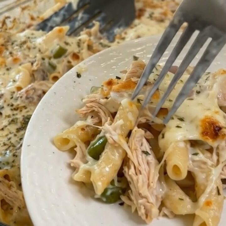 Mississippi chicken casserole with pasta and melted cheese lifted from a glass baking dish with a spatula, steam rising
