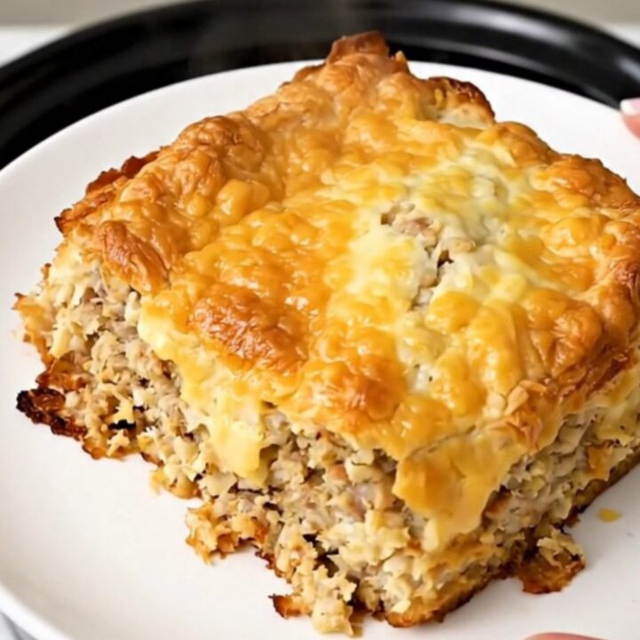 Golden crockpot sausage hash brown breakfast casserole steaming in a black oval slow cooker on a white countertop