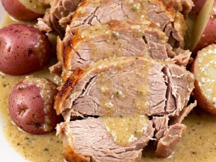 Sliced creamy ranch pork roast with halved red potatoes and glossy sauce on a white plate, steaming
