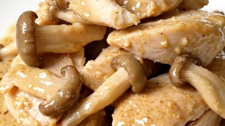Tender slow cooker chicken breasts on a white plate under a glossy cream and oyster mushroom sauce, steaming