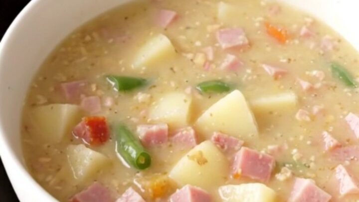 Creamy crockpot ham, green bean and potato soup steaming in a white bowl on a beige counter