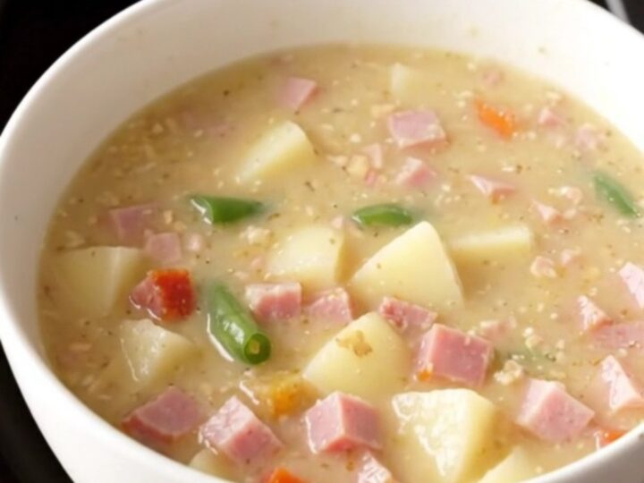 Creamy crockpot ham, green bean and potato soup steaming in a white bowl on a beige counter