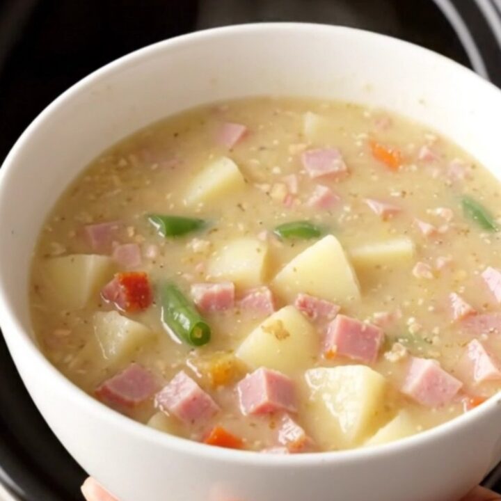 Creamy crockpot ham, green bean and potato soup steaming in a white bowl on a beige counter