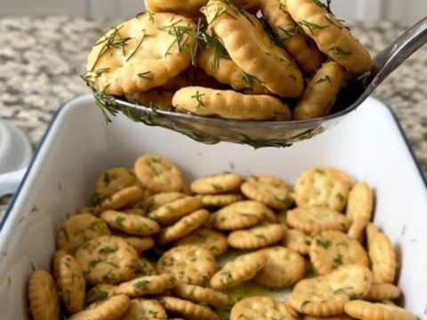 Toasted dill pickle oyster crackers coated in garlic dill butter, heaped on a large serving spoon over a white baking dish