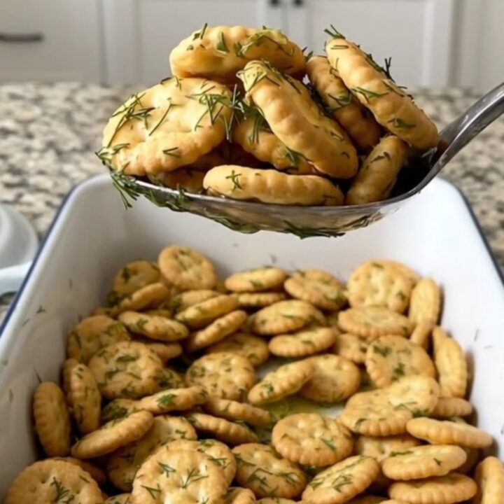 Toasted dill pickle oyster crackers coated in garlic dill butter, heaped on a large serving spoon over a white baking dish