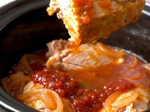 Whole turkey tenderloins coated in glossy red pepper jelly sauce with onion half-moons in a slow cooker insert