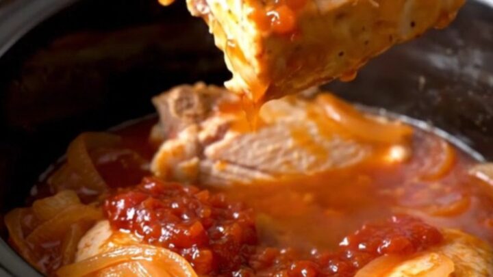 Whole turkey tenderloins coated in glossy red pepper jelly sauce with onion half-moons in a slow cooker insert