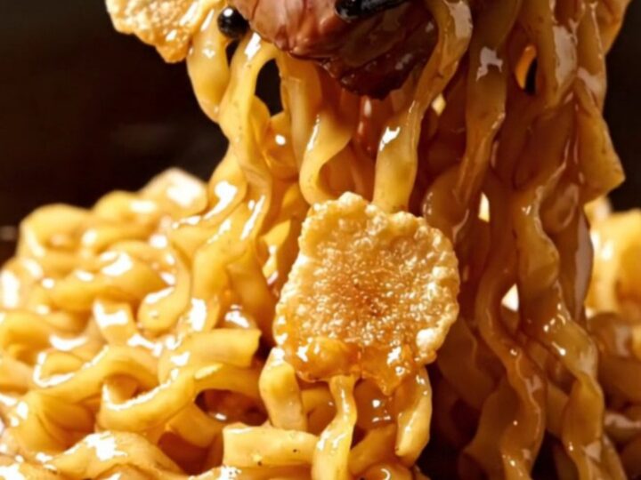Seared Wagyu ribeye cubes with crispy garlic chips over glossy soy-butter ramen noodles in a dark bowl