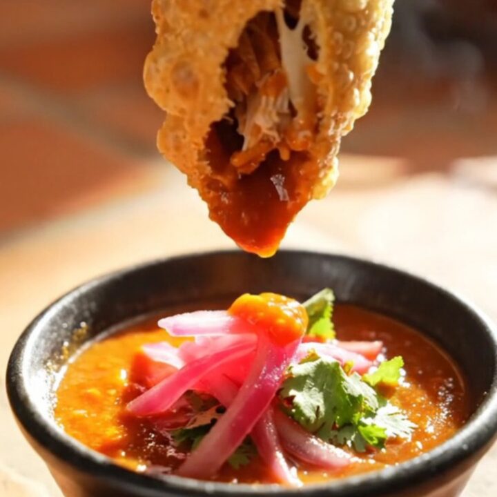 Golden blistered chicken birria empanada broken in half with molten Monterey Jack stretching and steam rising