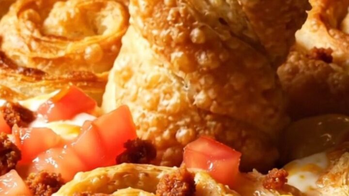 Golden crispy tortilla cheese twists piled beside a bubbling skillet of white queso topped with tomatoes and chorizo