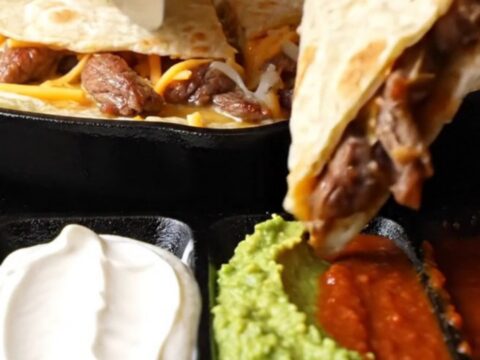 Golden steak fajita quesadilla triangle lifted with long strands of melted Oaxaca and cheddar cheese