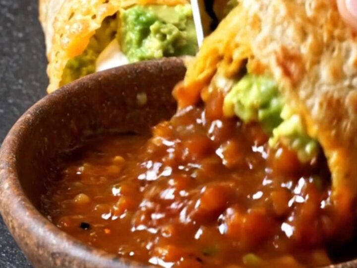 A halved burrito wrapped in a golden baked cheddar shell showing steak, guacamole and sour cream layers