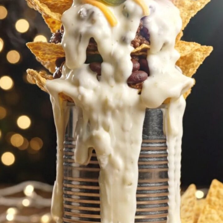 Towering trash can nachos with layers of chips, taco beef, black beans and molten white queso cascading down a platter