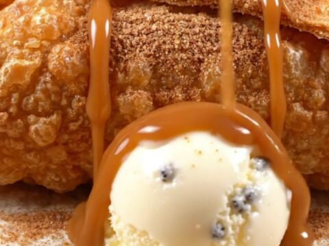 A crispy apple pie chimichanga cut open, spiced apples and caramel spilling out beside melting vanilla bean ice cream