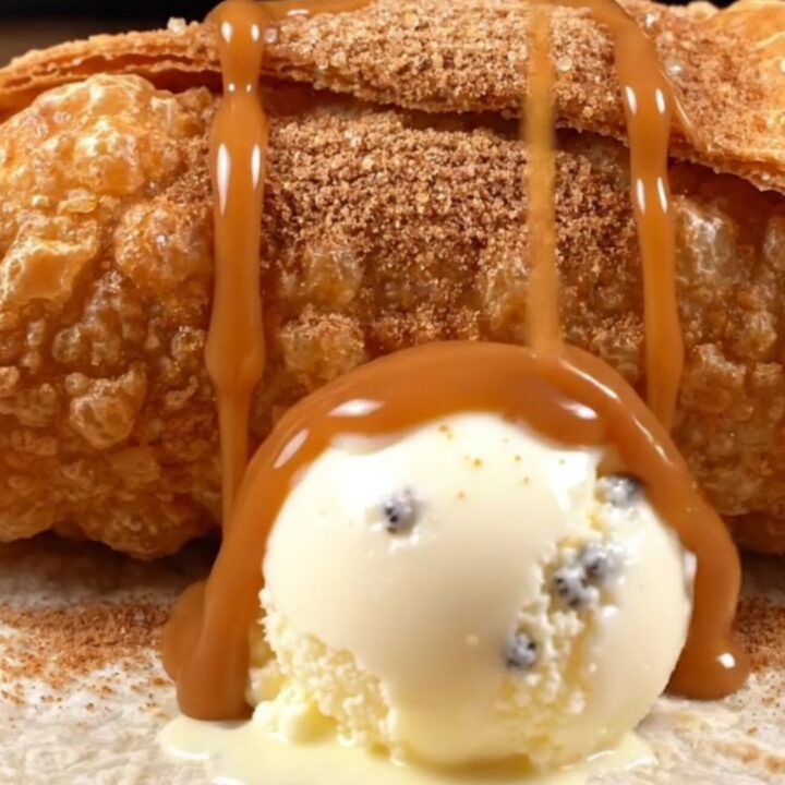 A crispy apple pie chimichanga cut open, spiced apples and caramel spilling out beside melting vanilla bean ice cream