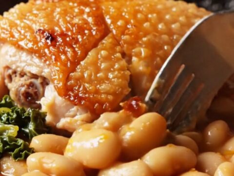 Crispy chicken thighs over creamy Spanish butter beans in brick-red chorizo oil with wilted kale in a cast-iron skillet