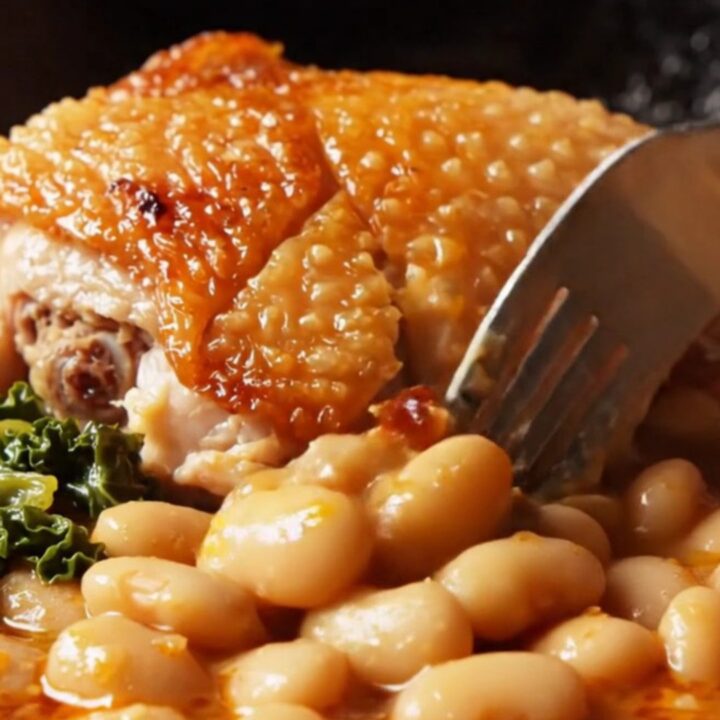 Crispy chicken thighs over creamy Spanish butter beans in brick-red chorizo oil with wilted kale in a cast-iron skillet