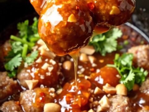 Glossy slow-cooker sweet Thai chili lime cocktail meatballs in a ceramic insert, garnished with cilantro and peanuts