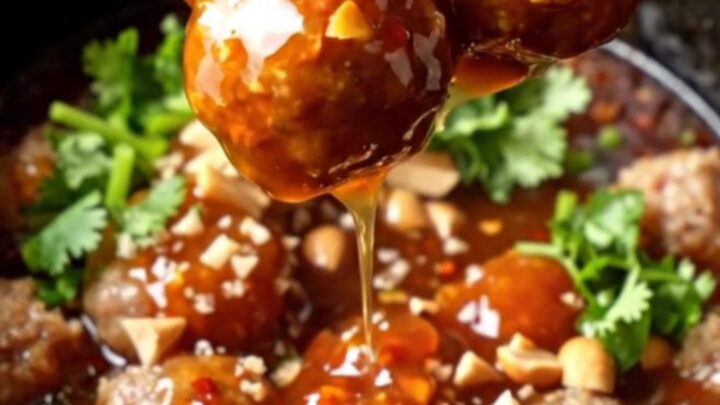 Glossy slow-cooker sweet Thai chili lime cocktail meatballs in a ceramic insert, garnished with cilantro and peanuts