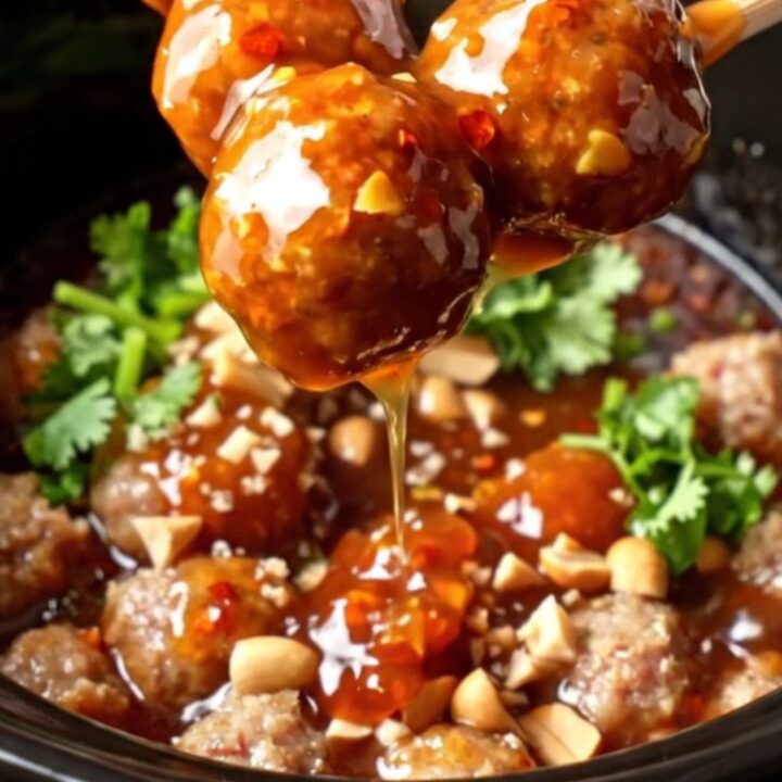 Glossy slow-cooker sweet Thai chili lime cocktail meatballs in a ceramic insert, garnished with cilantro and peanuts