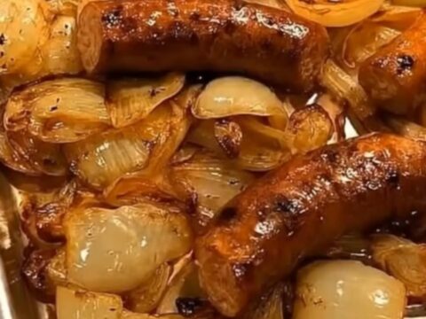 Browned roasted sausages on a bed of glossy caramelized onions on a white plate, steam rising
